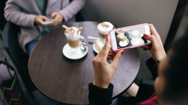 Someone photographs two coffees on a café table with a phone.