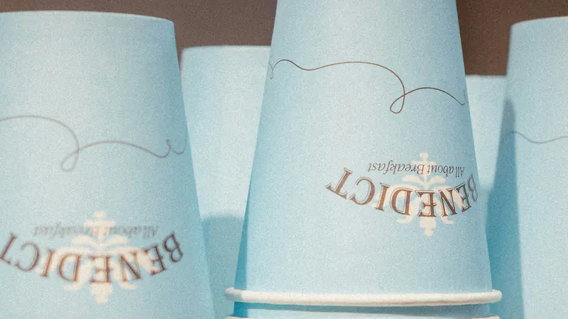 Stacks of light blue paper cups, each printed with the same logo.