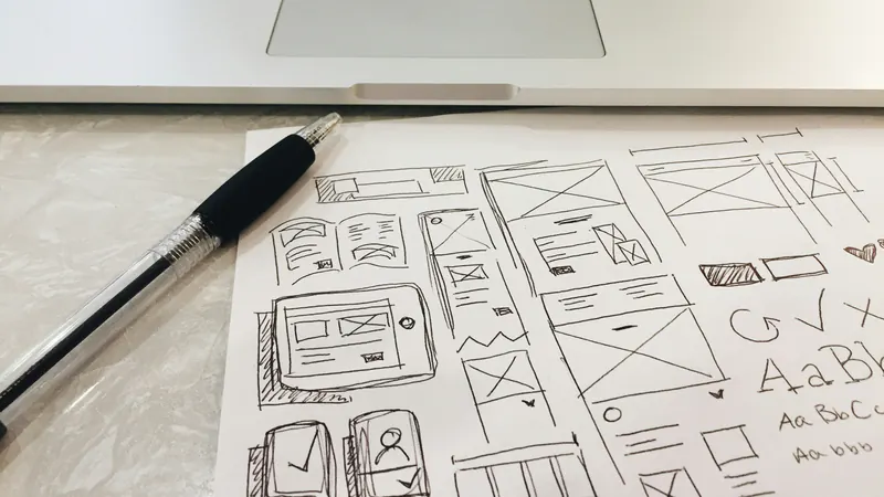 Hand-drawn sketches of a website’s screens beside a laptop and a pen.